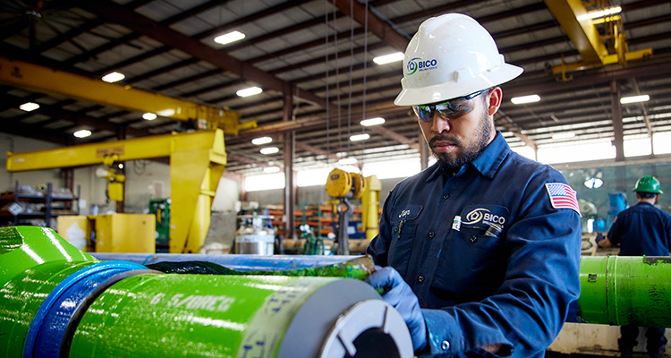 worker performing quality control or maintenance on a large, green cylindrical component